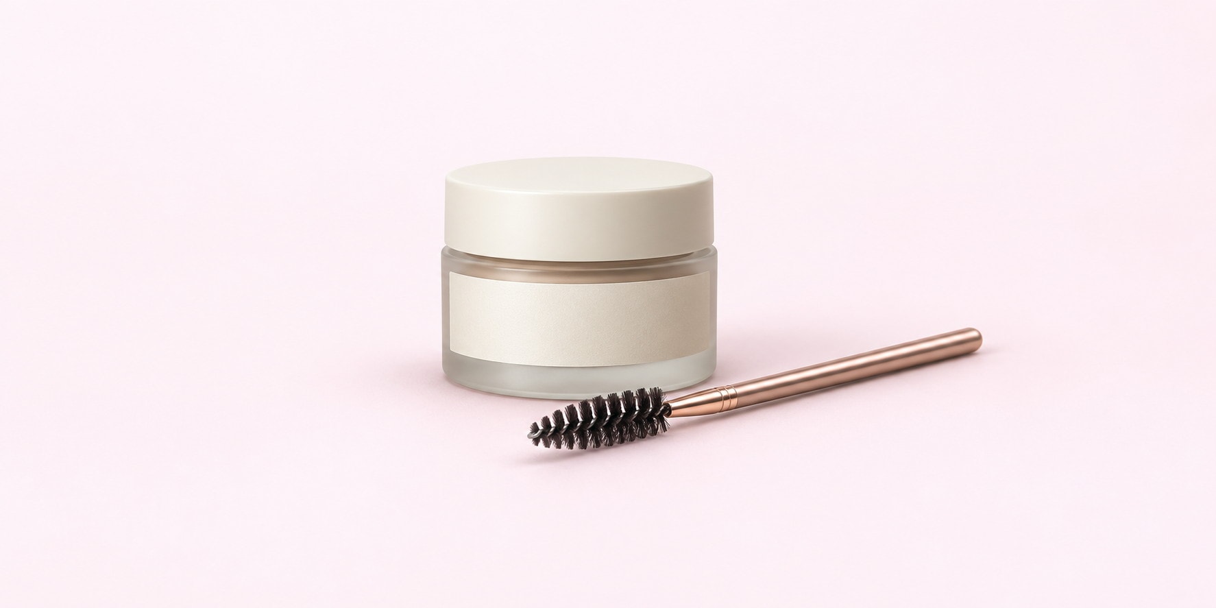 A frosted balm jar beside a rose gold spoolie, shot on pink